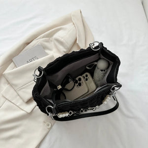 Black textured grid pearl chain tote bag with pearl and flower charms, showing interior contents.
