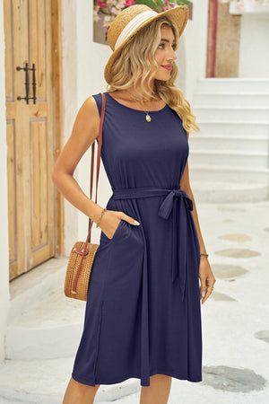 Sleeveless midi dress in dark blue with belted waist, pockets, and slit hem.