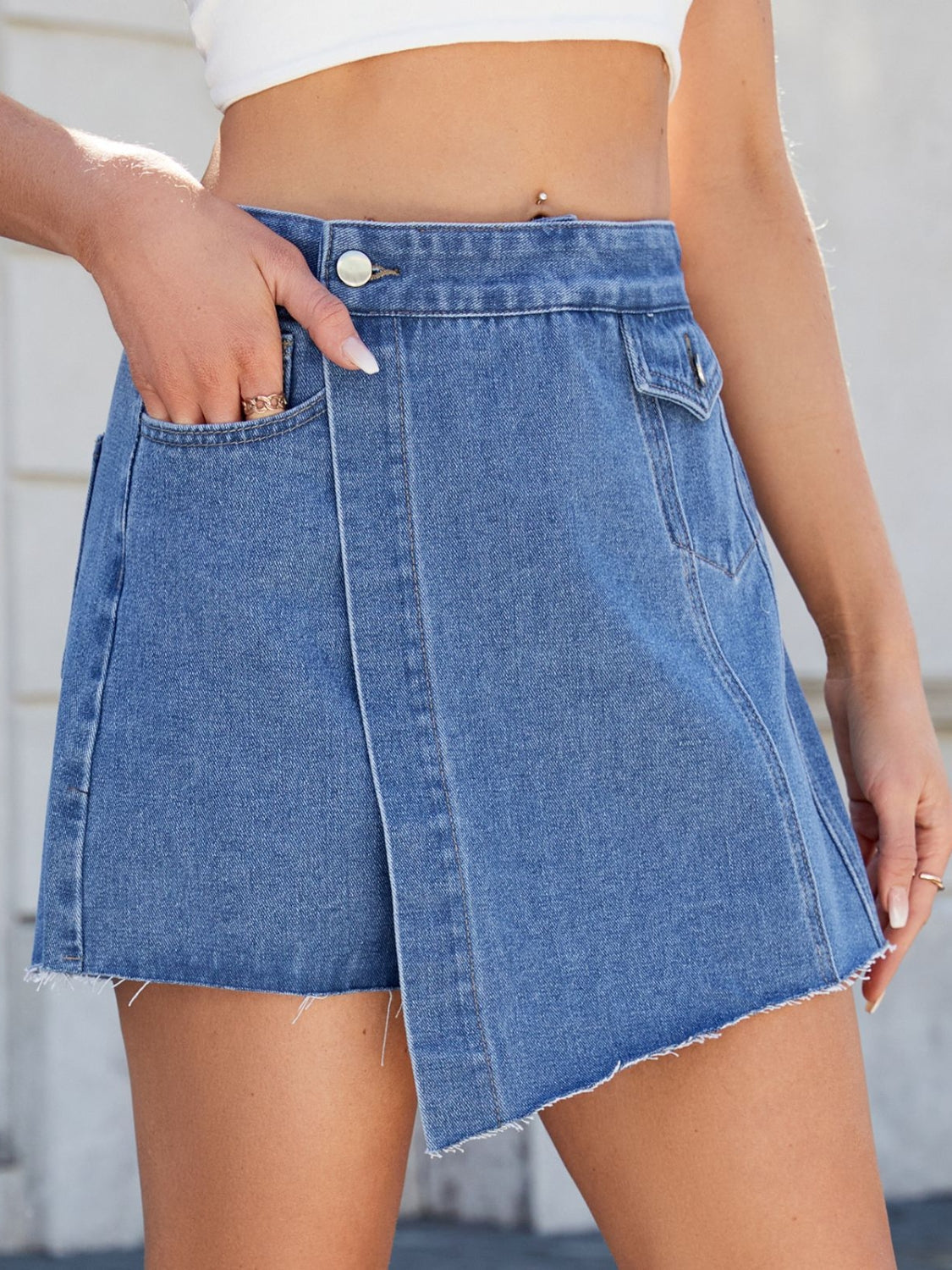 Medium wash denim skort with asymmetric wrap and raw hem detail