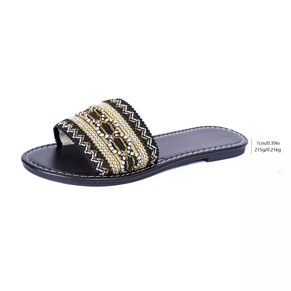Black artisan slide sandals with intricate gold and white bead embroidery on the strap.