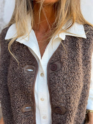 Coffee brown teddy bear vest with leather trim and button closure, worn over white shirt.