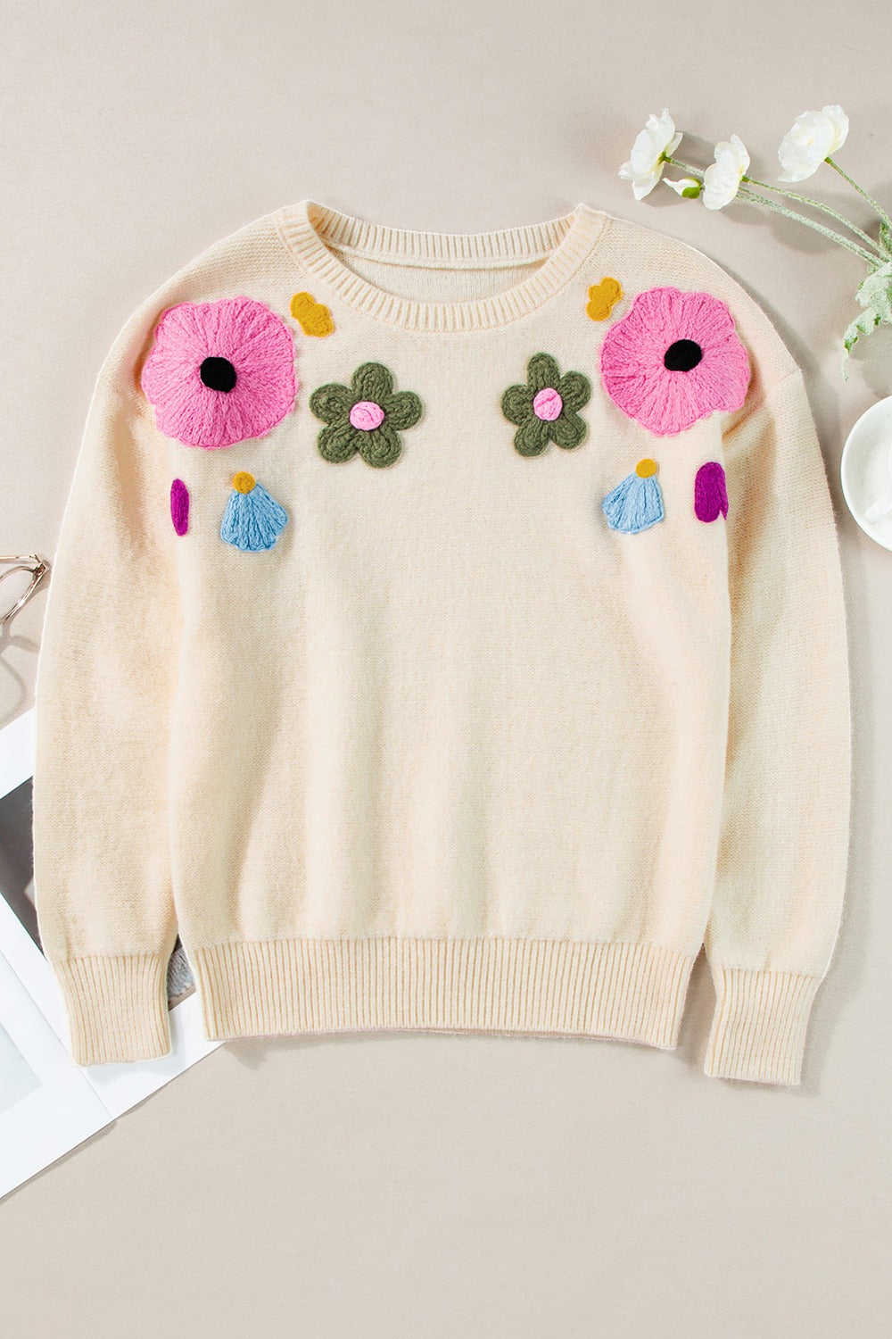 Cream knit sweater with embroidered floral appliqués and ribbed trim.
