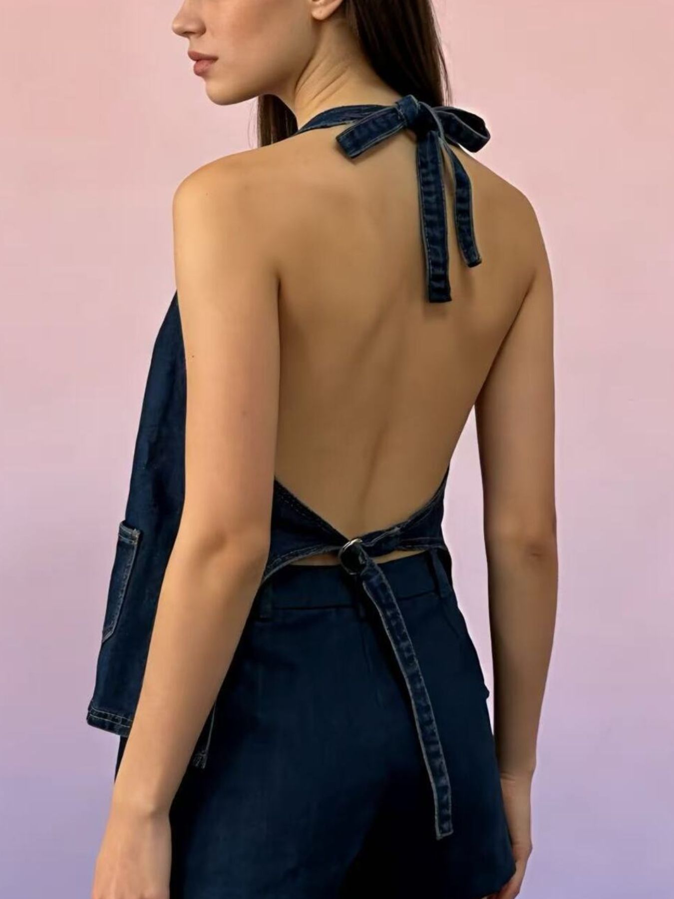 Button-down denim halter vest in dark blue with a tie back and pocket detail.