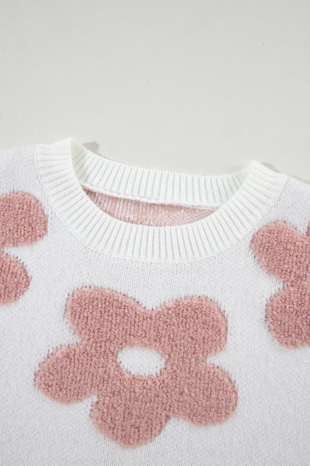 White knit pullover with textured pink floral pattern and crew neck.