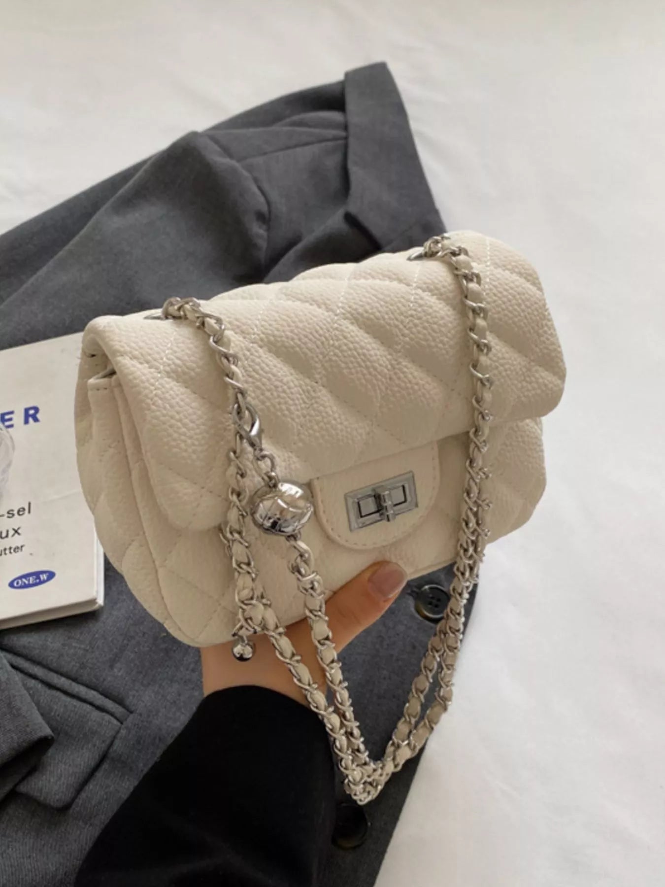 Quilted chain crossbody clutch in rice white with silver hardware and a turn-lock closure.