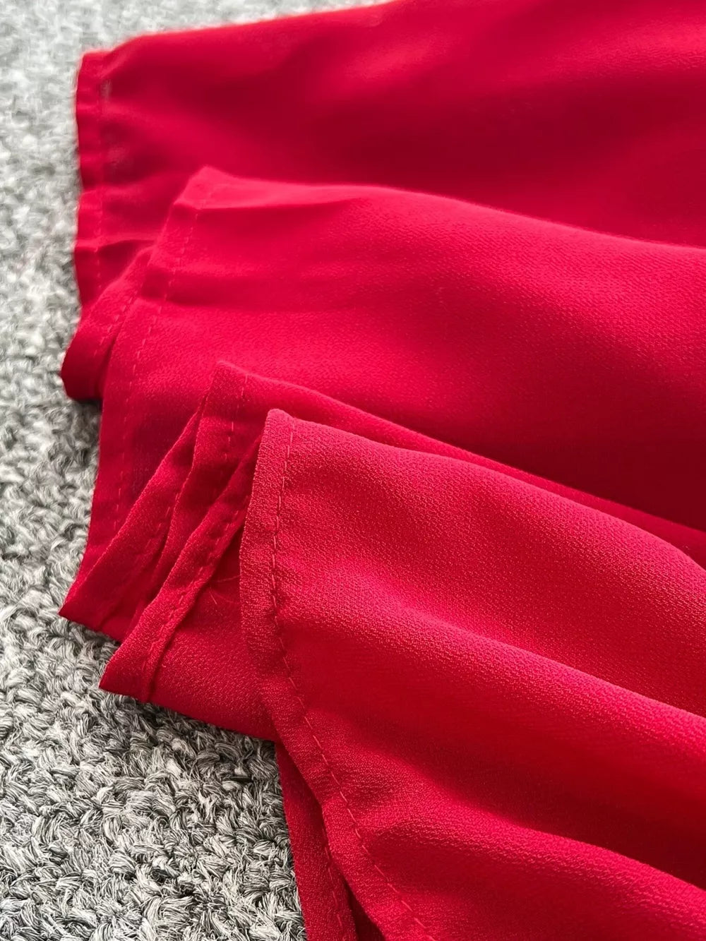 Red maternity maxi dress with one-shoulder neckline and floral accents, shown in a close-up of the fabric.