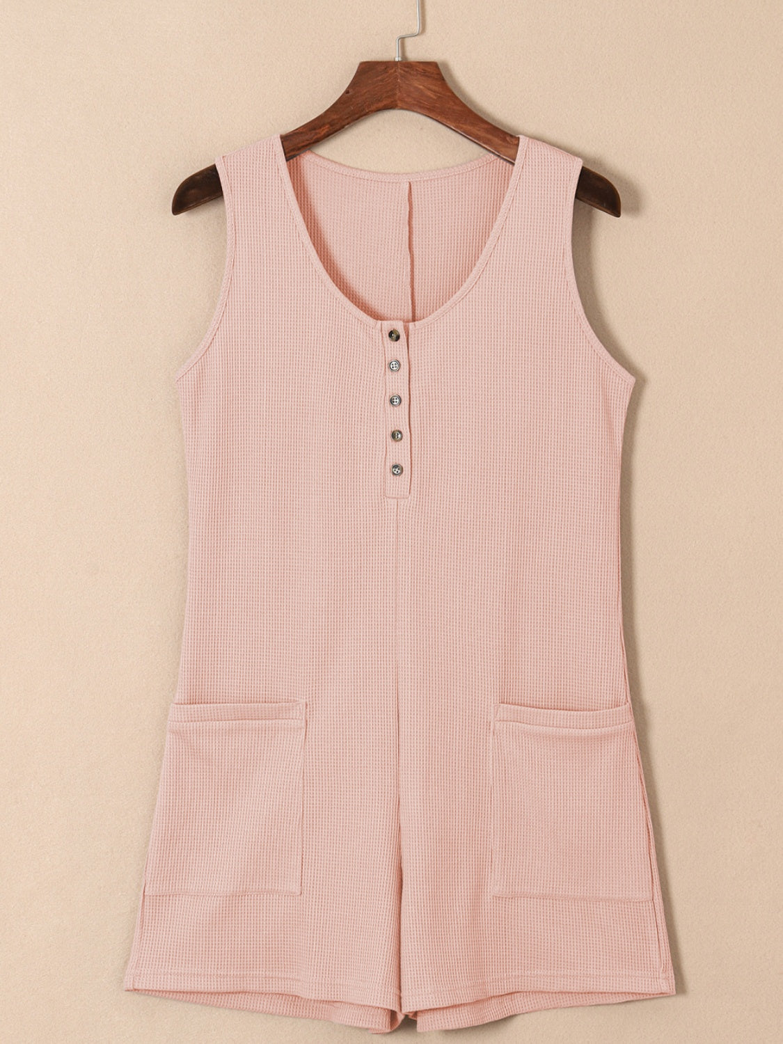 Blush pink waffle knit button-down romper with pockets and a scoop neckline.