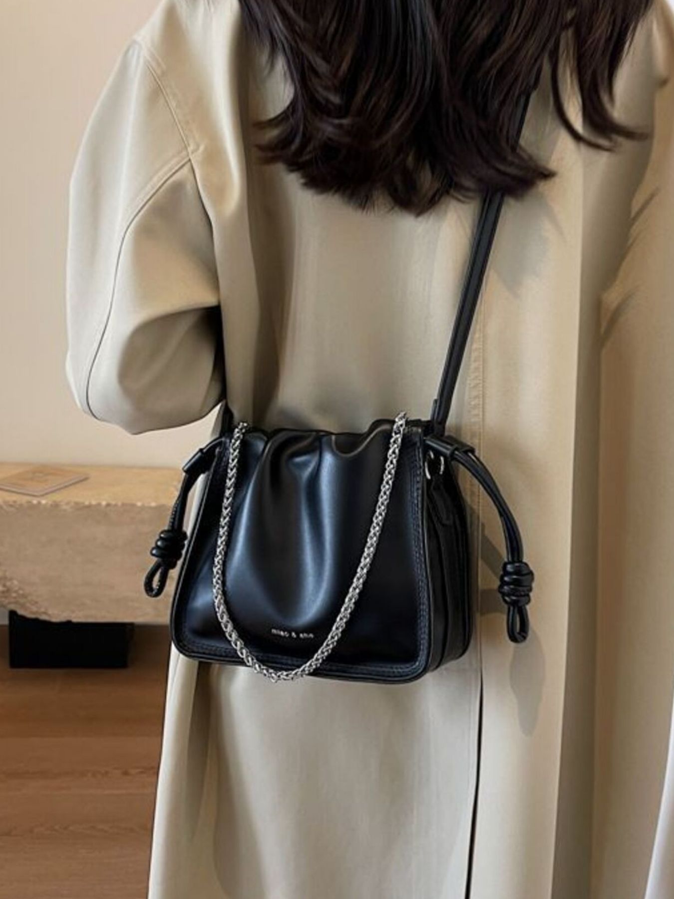 Black ruched PU leather crossbody bag with silver chain detail and knotted strap accents.