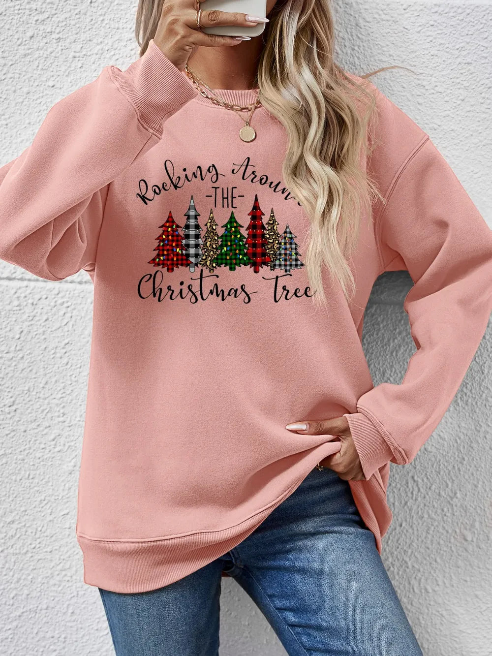 Blush pink crewneck sweatshirt with a graphic Christmas tree print and text that reads Rocking Around the Christmas Tree.