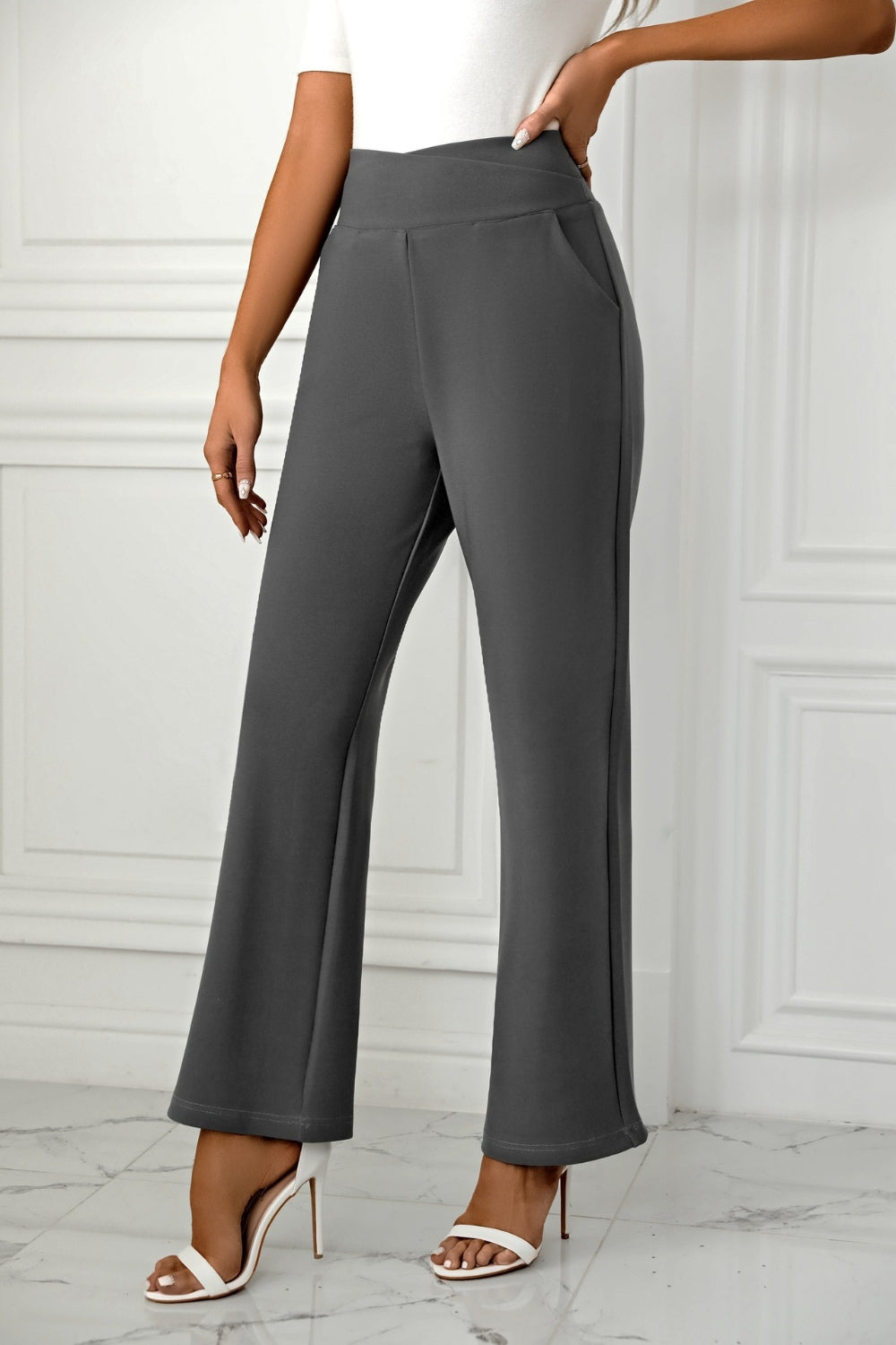 Dark gray wide-leg trousers with a sculpted waist and pockets, styled with white heels.