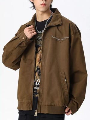 Brown cotton zip-up jacket with embroidered detail and pockets, worn open over a graphic tee.