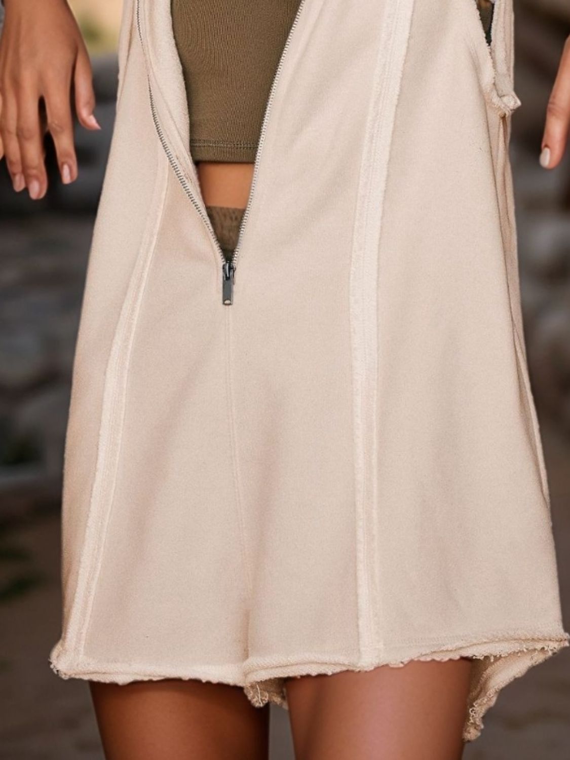 Tan sleeveless hooded romper with raw edges and a zippered front.