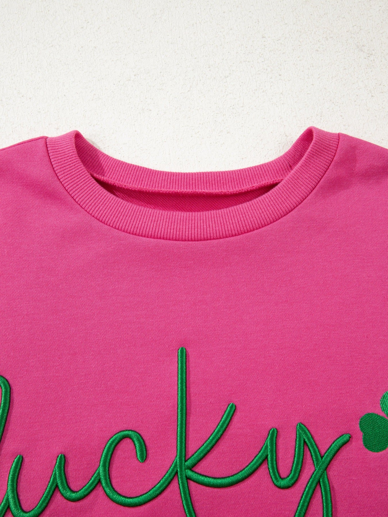 Pink crew neck sweatshirt with embroidered green lucky clover and script text detail.
