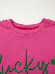 Pink crew neck sweatshirt with embroidered green lucky clover and script text detail.