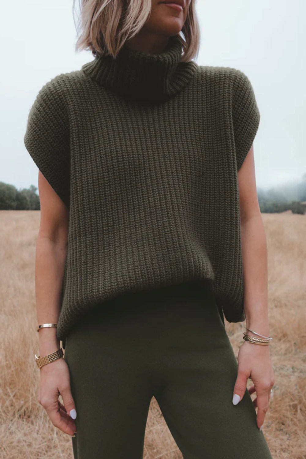 Sleeveless ribbed turtleneck sweater in army green acrylic, styled casually.