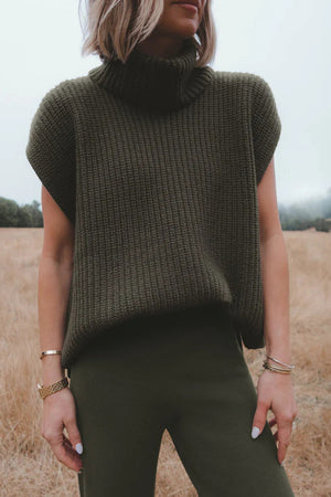 Sleeveless ribbed turtleneck sweater in army green acrylic, styled casually.