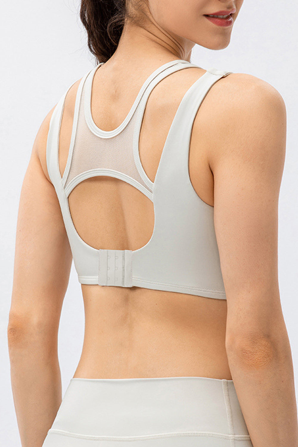 Mesh inset performance bra top in light gray with strappy back detail and hook closure.