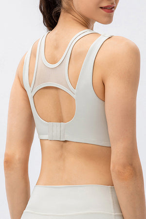 Mesh inset performance bra top in light gray with strappy back detail and hook closure.