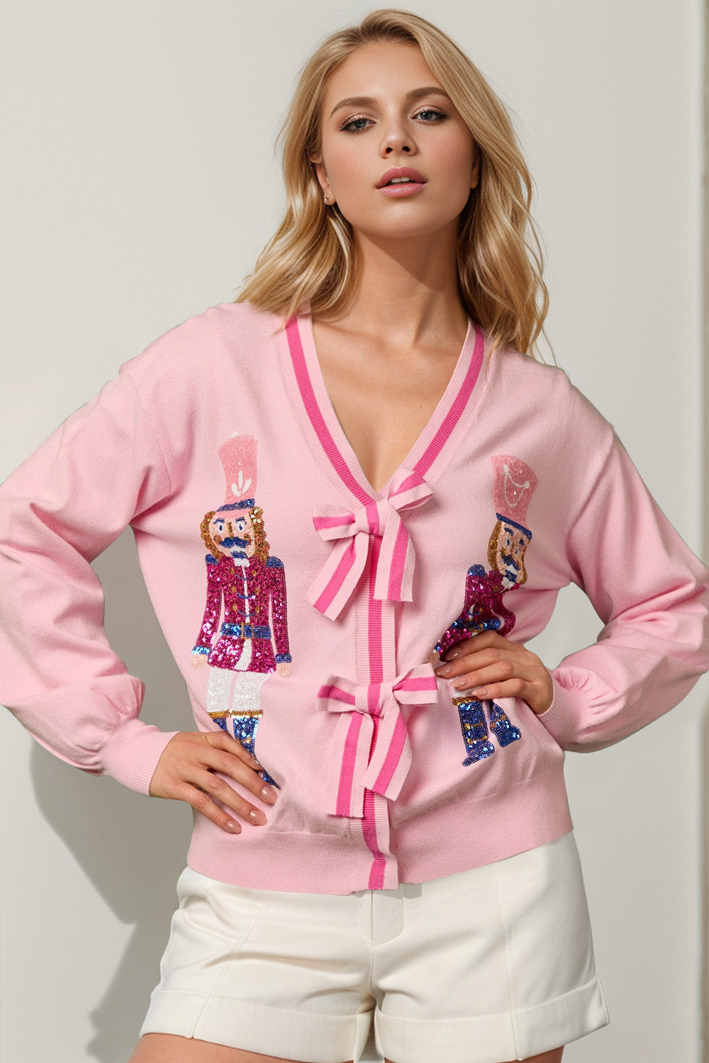 Blush pink cardigan with sequin nutcracker embellishments and bow-tie closures.