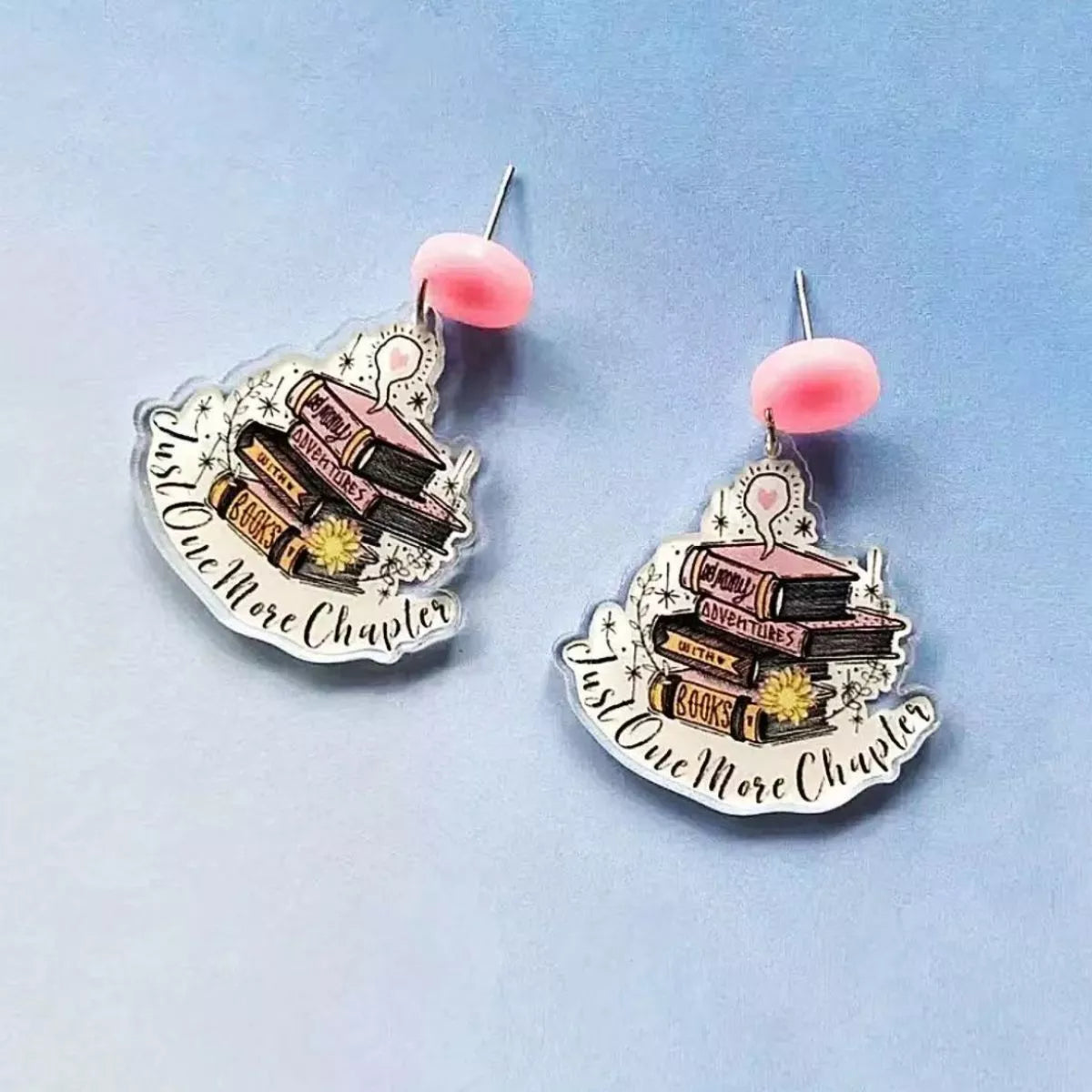 Book stack acrylic drop earrings in blush pink with "Just One More Chapter" text.