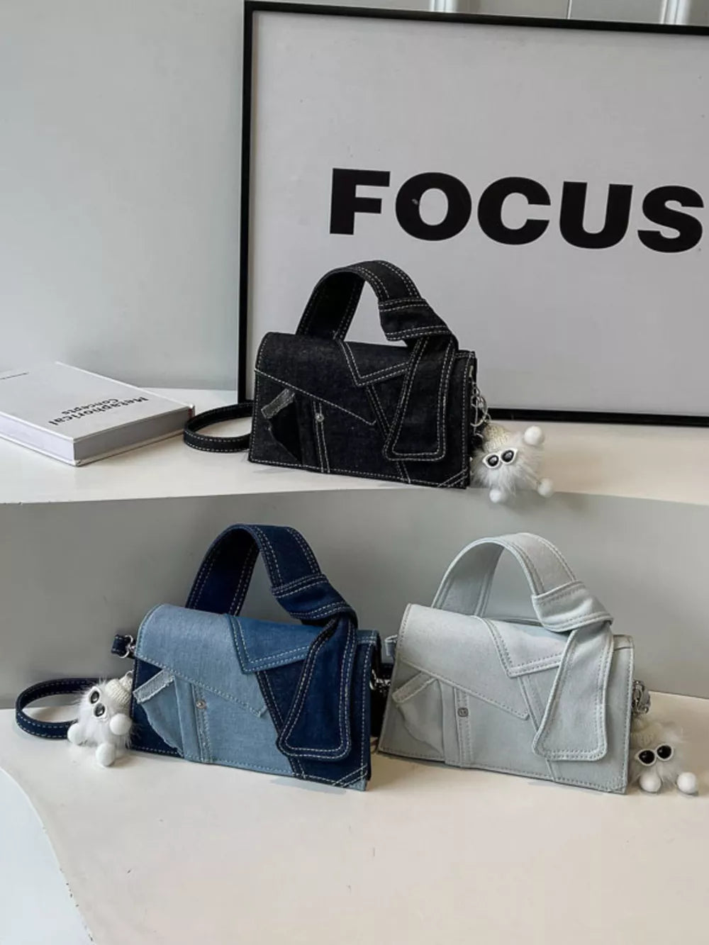 Artisanal denim crossbody bag in black, light blue, and off-white with contrast stitching and a fluffy charm.