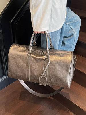 Textured metallic duffle bag in champagne color with detachable strap and luggage tag.
