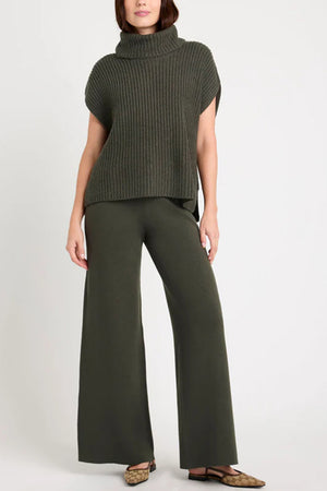 Sleeveless ribbed turtleneck sweater in army green acrylic, styled with wide-leg pants.