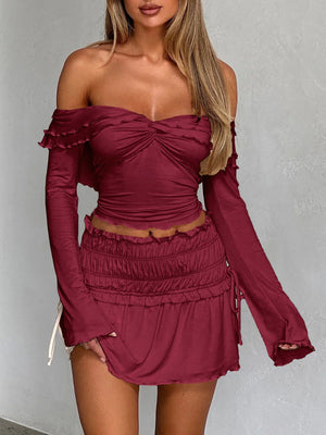 Ruched bodice off-shoulder top in rust with ruffled neckline and long sleeves.