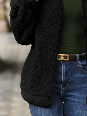 Black textured teddy zip-up jacket with quilted pattern, worn open over a green top and jeans.