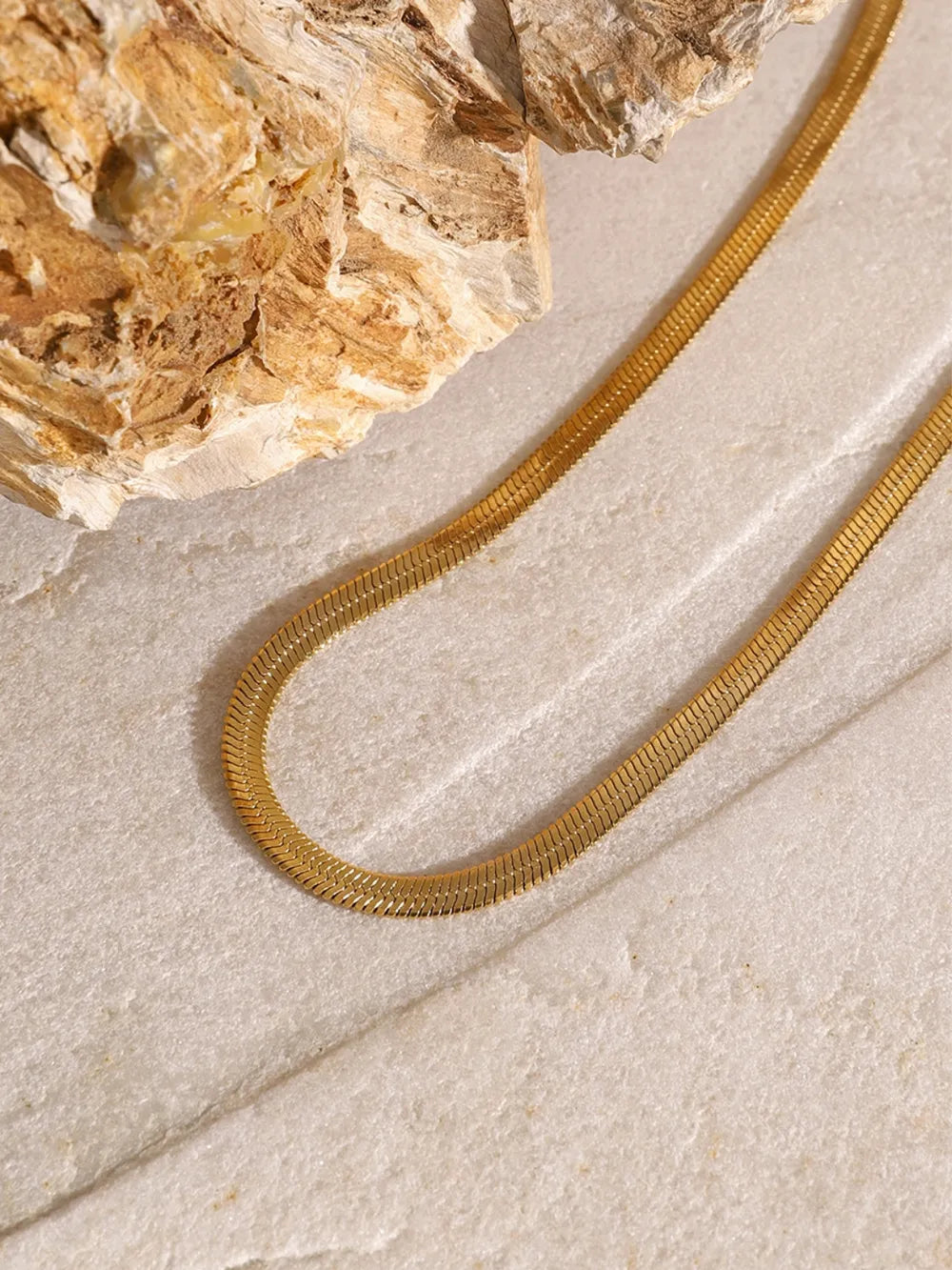Gold layered necklace with a flat serpentine chain and a cross pendant.