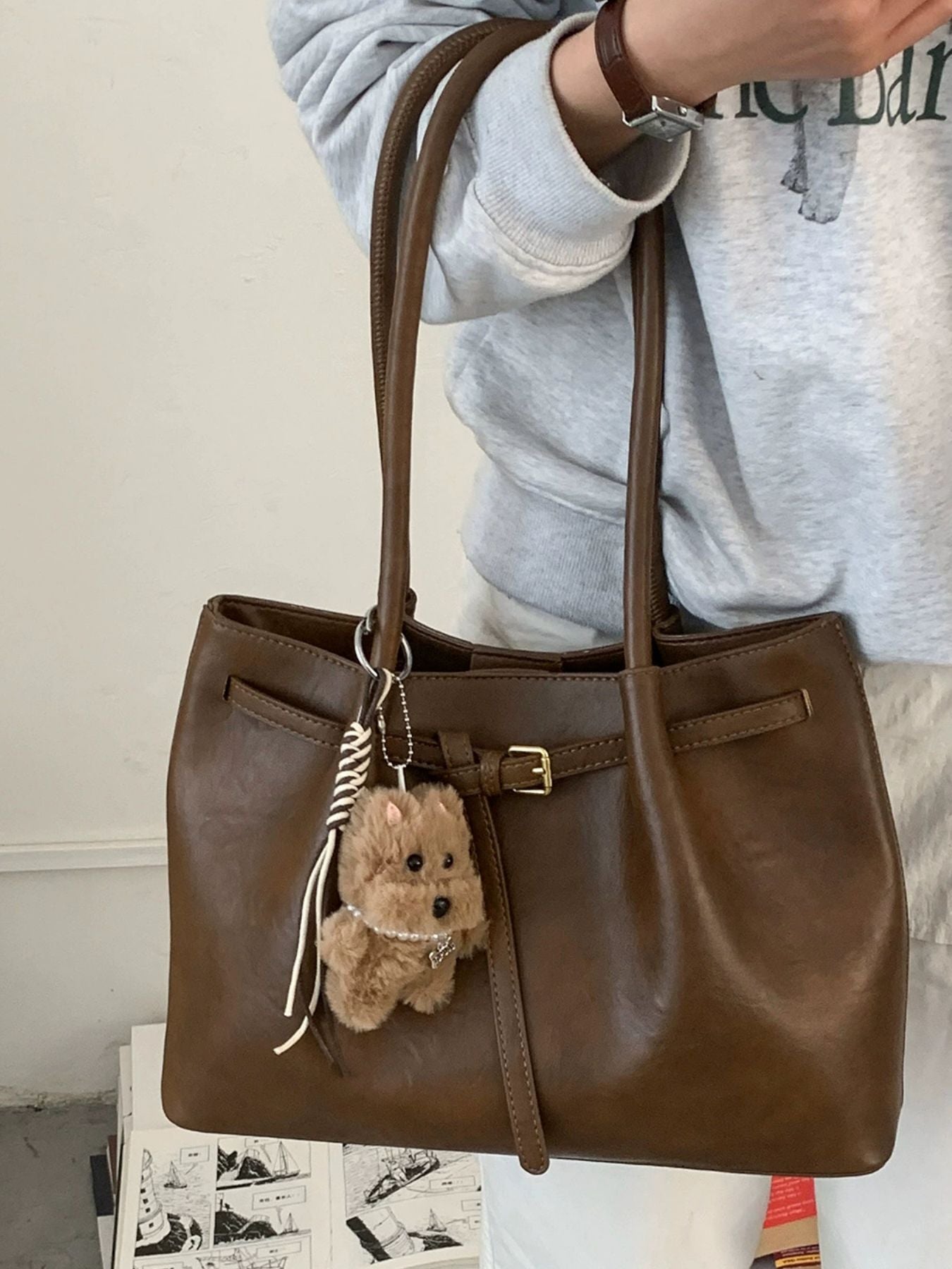 Brown leather shoulder bag with buckle detail and a fluffy dog charm