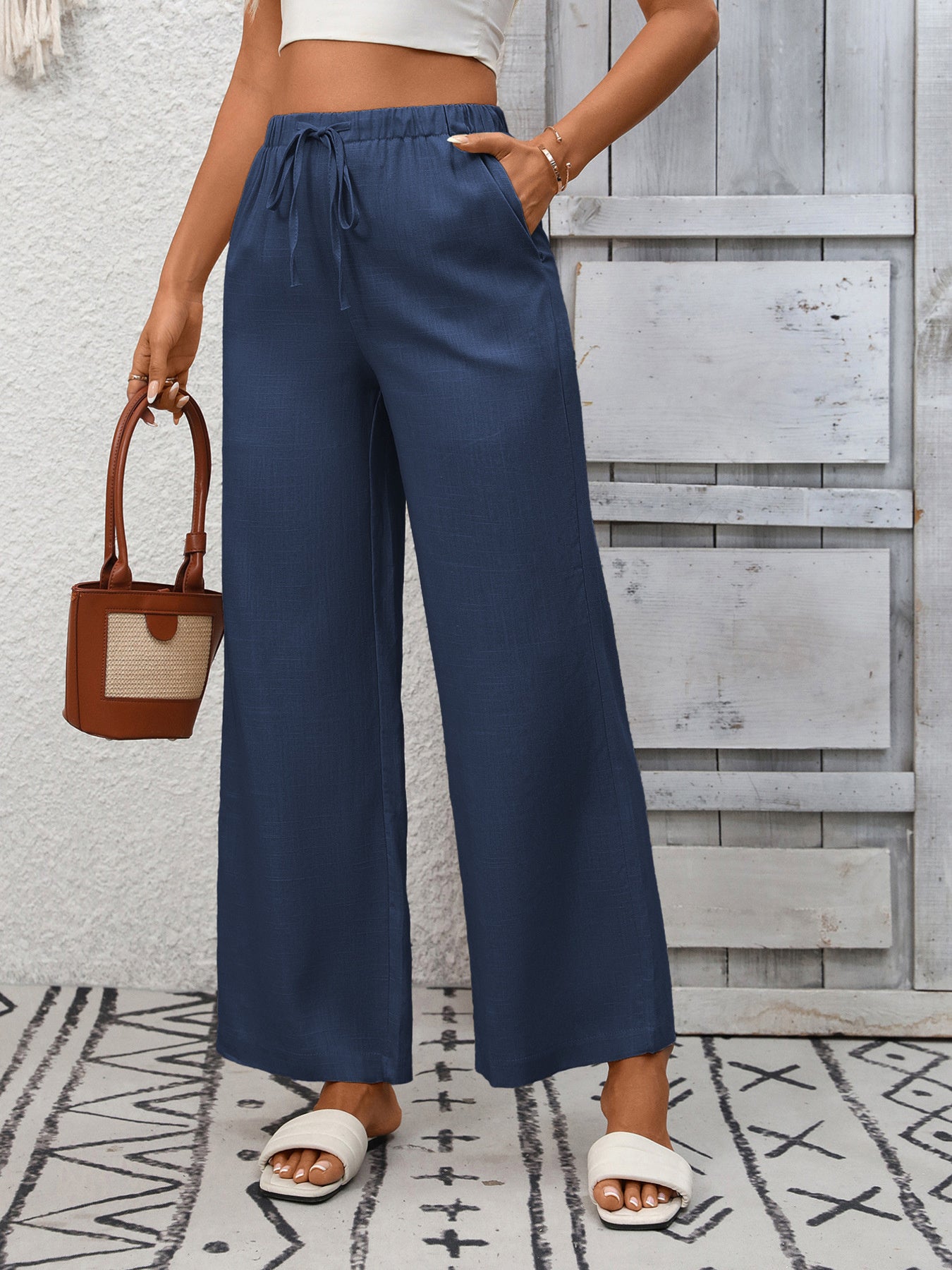 Navy blue wide-leg drawstring pants with pockets, styled with white slides and a small bag.