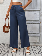 Navy blue wide-leg drawstring pants with pockets, styled with white slides and a small bag.