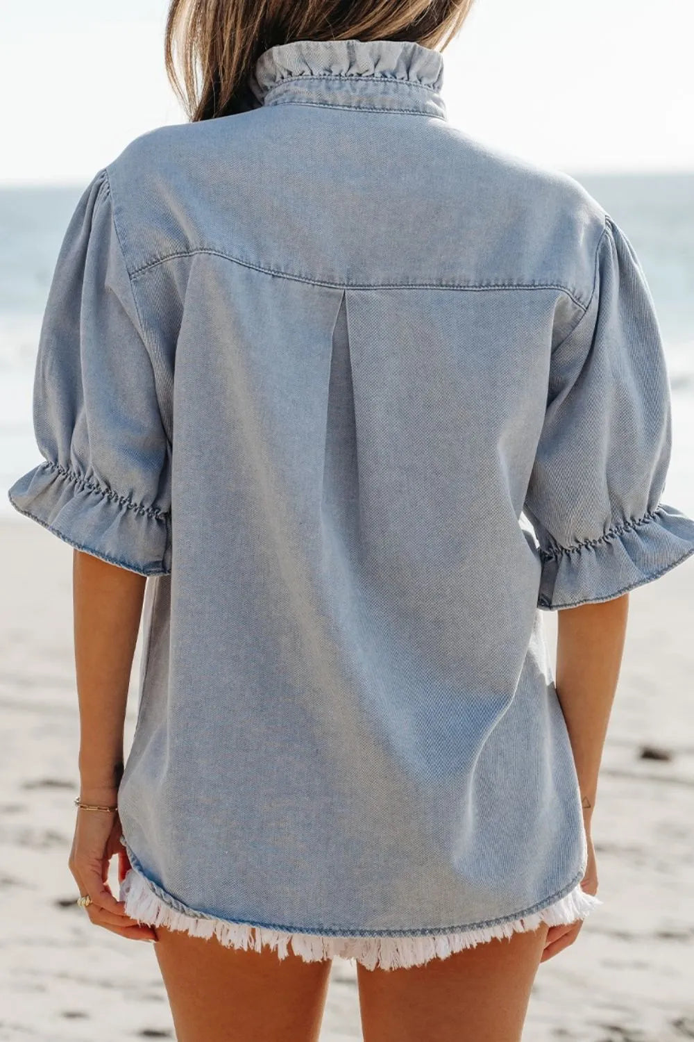 Light blue denim blouse with ruffled collar, puff sleeves, and frayed hem.