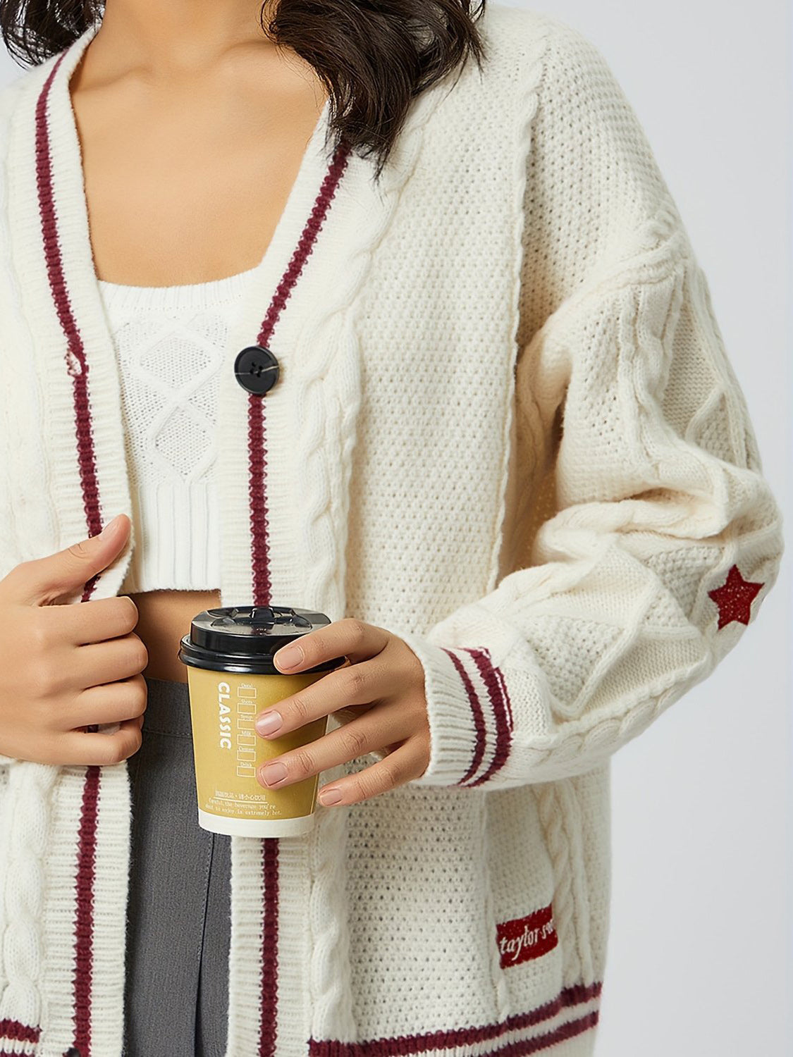 White cable knit cardigan with burgundy stripes and star detail on sleeve.