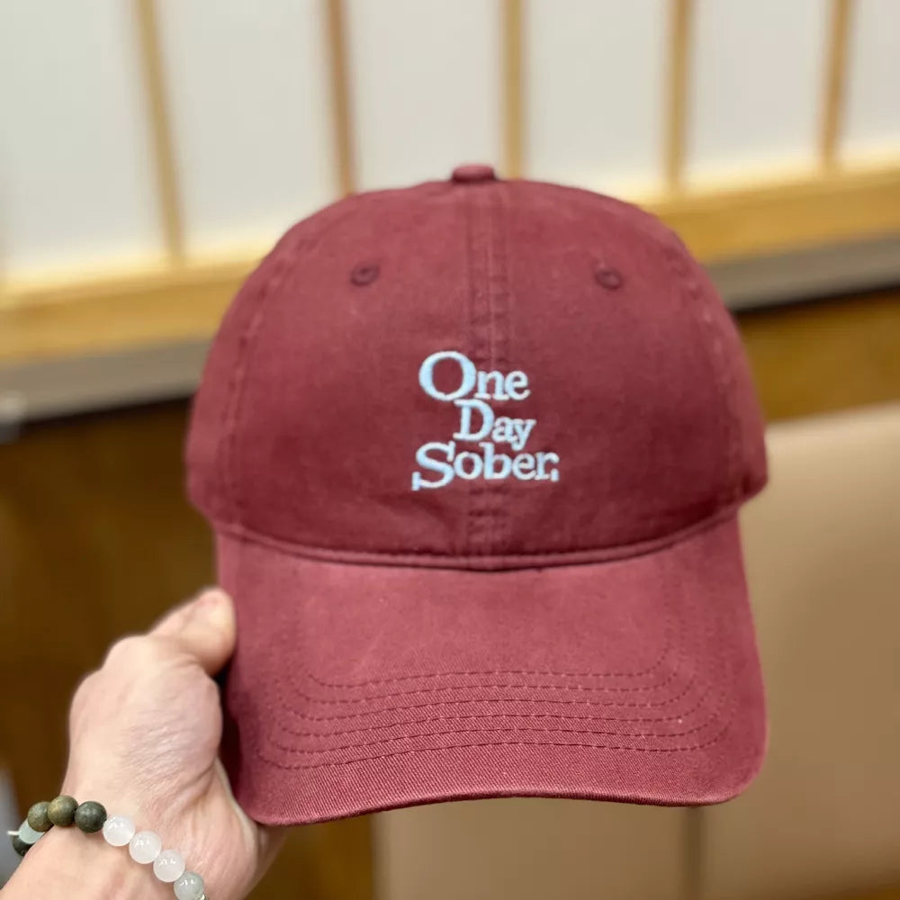 Wine red cotton baseball cap with distressed finish and embroidered "One Day Sober" text.
