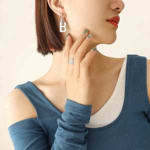 Silver letter B statement hoop earrings made of titanium, worn with a layered blue top.