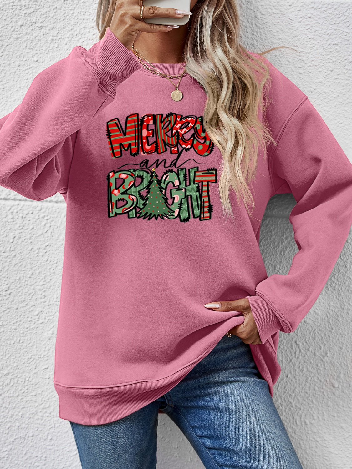 Blush pink crewneck sweatshirt with Merry and Bright Christmas graphic and tree detail.