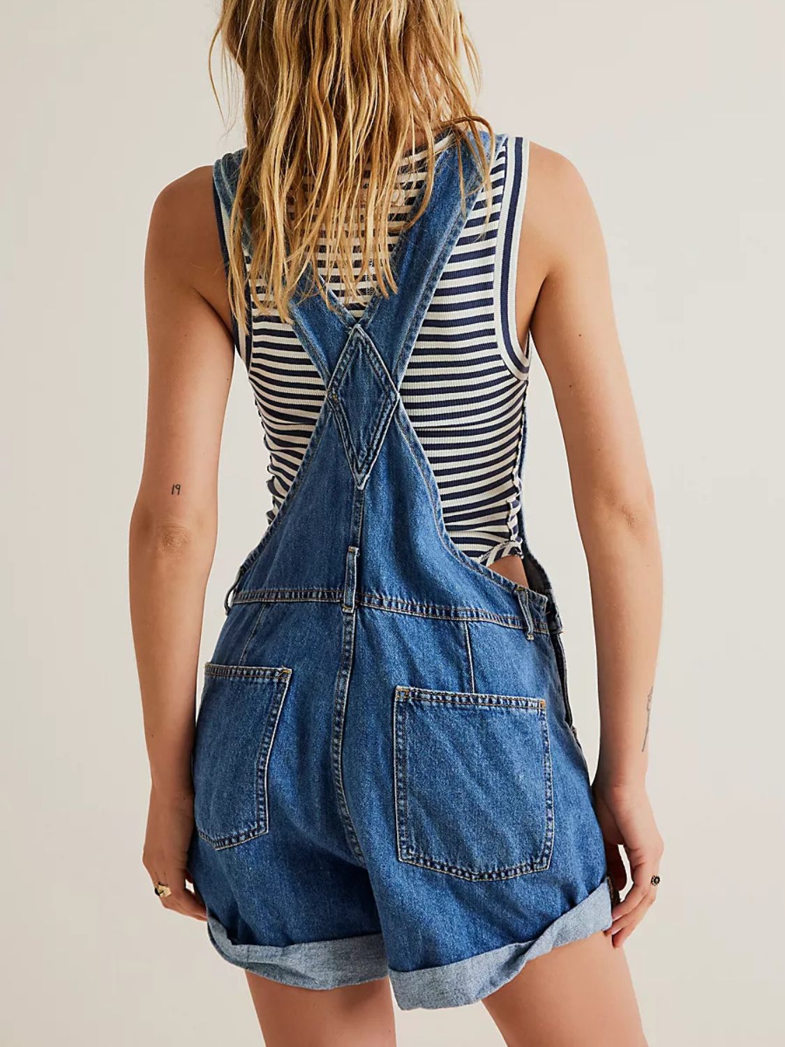 Medium wash denim overalls with cuffed shorts and a striped tank top.
