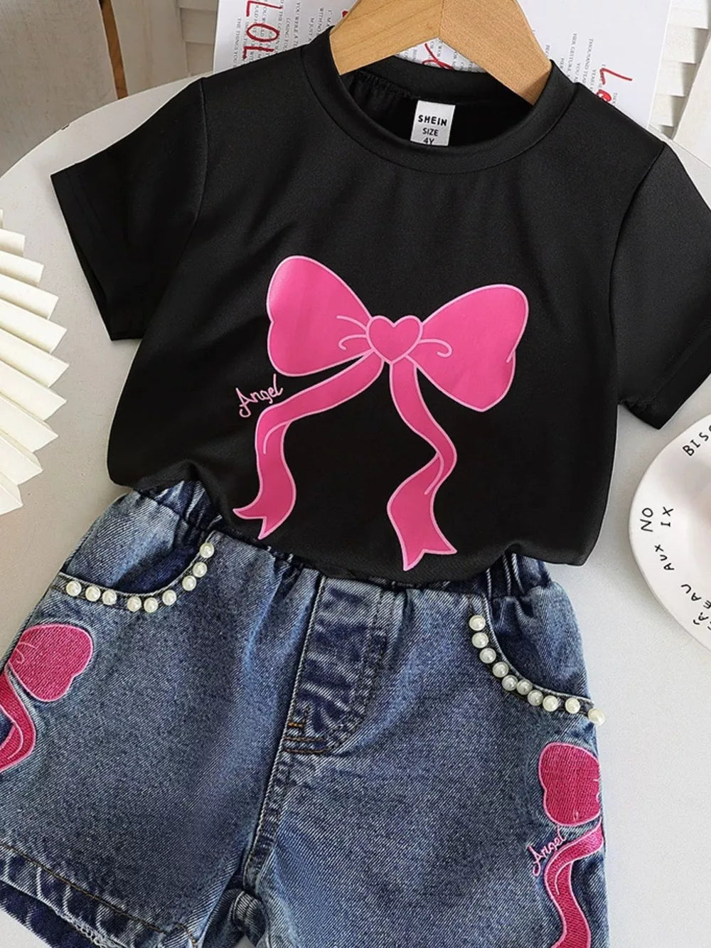 Black tee with pink bowknot graphic and pearl-trimmed denim shorts.