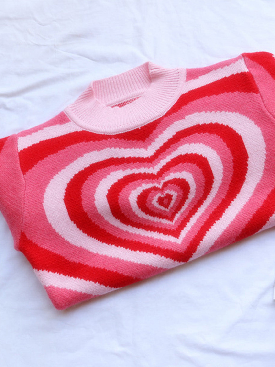 Pink knit sweater with mock neck and concentric heart stripe pattern in red and light pink.