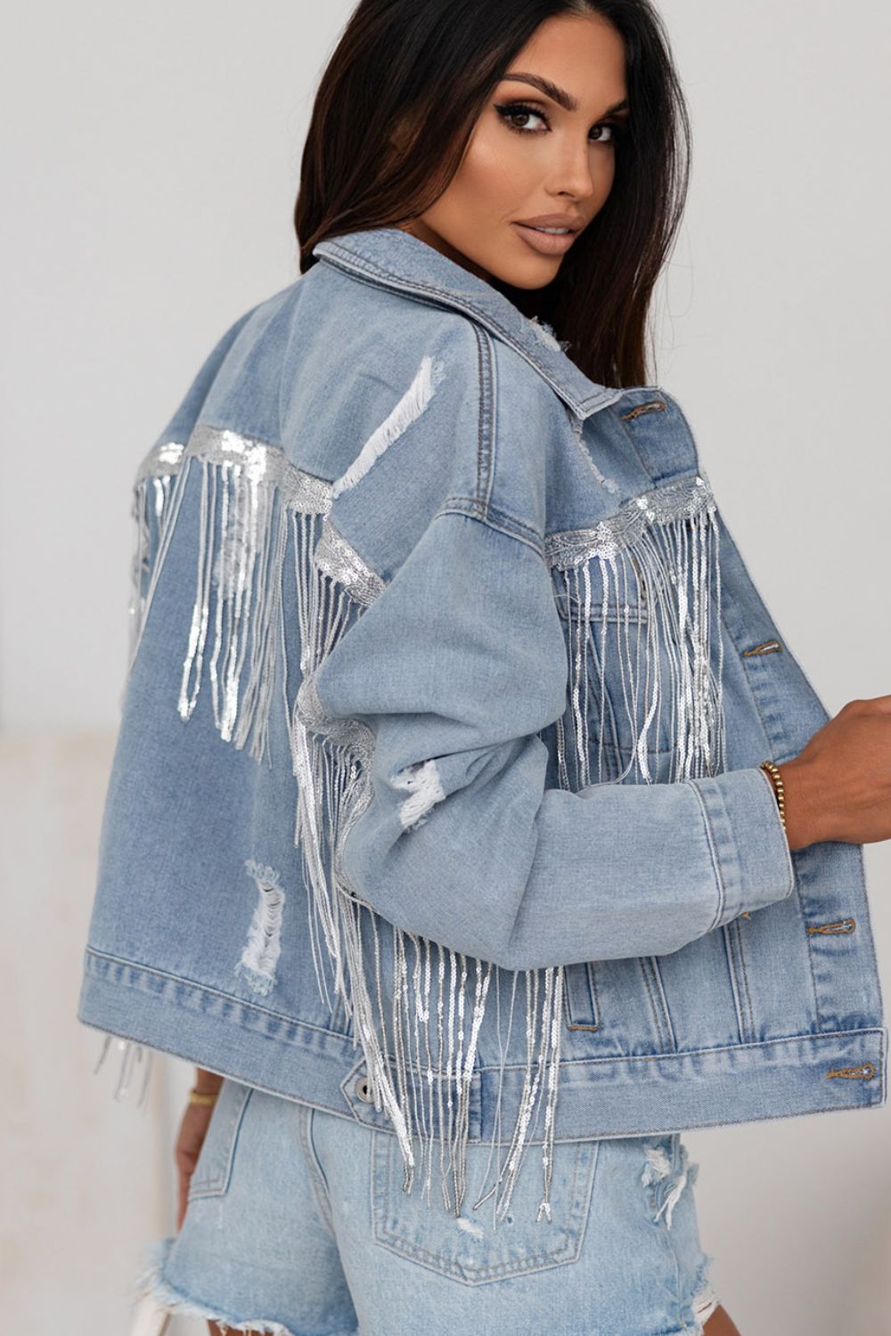 Denim trucker jacket in medium wash with distressed details and silver sequin fringe accents.