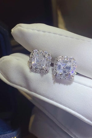 Silver asscher cut halo stud earrings with sparkling cubic zirconia on white fabric.