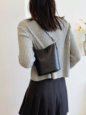 Black leather bucket crossbody bag with a subtle embossed logo detail.