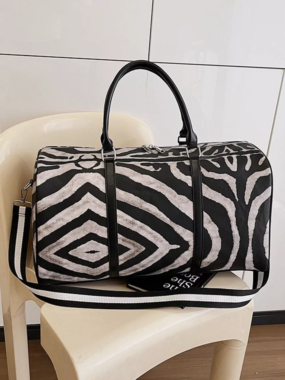 Large black and white zebra print duffle bag with carry handles and detachable strap.