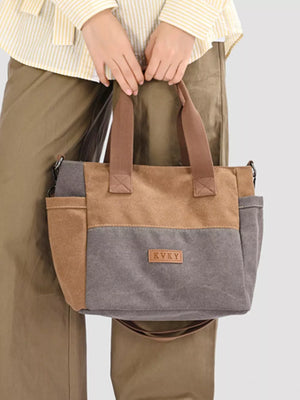 Multi-pocket canvas travel bag in dark gray and taupe with brown straps and adjustable strap.