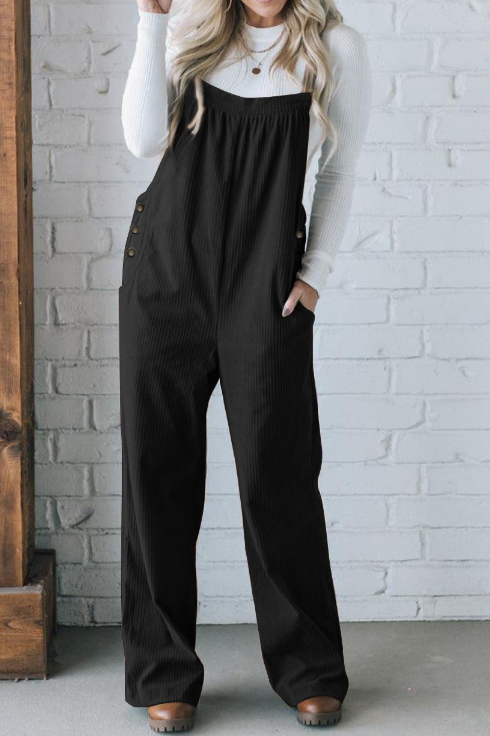 Black corduroy wide-leg overalls with button details and pockets, styled with a white long-sleeve shirt.