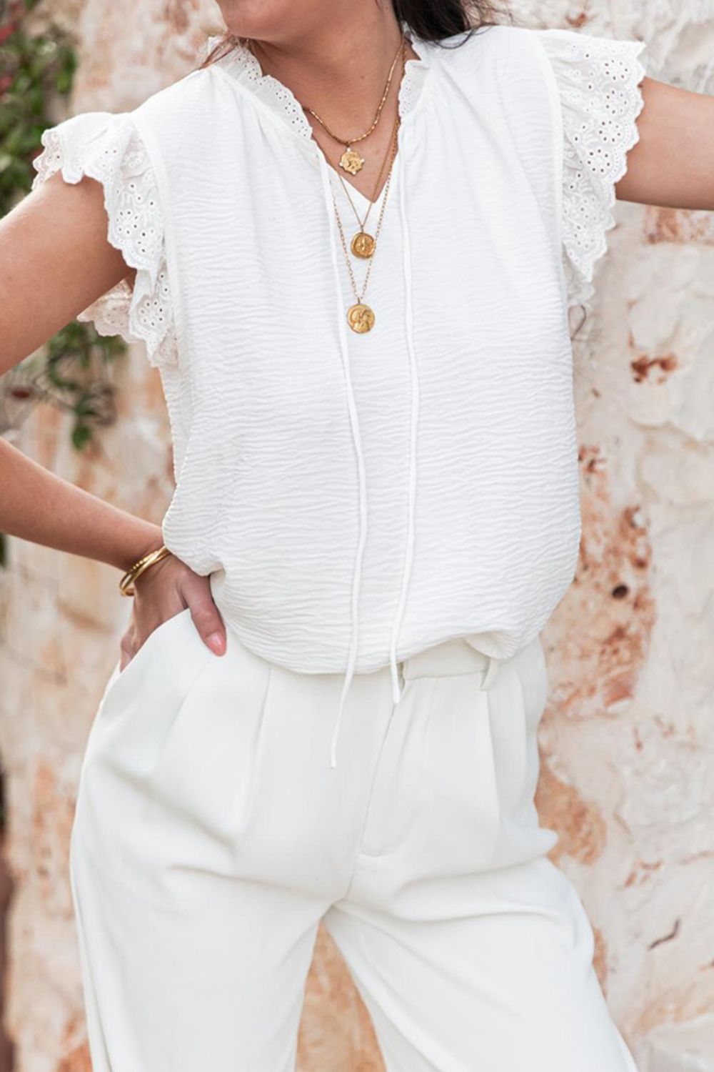 White textured tie-neck blouse with eyelet trim flutter sleeves and a relaxed fit.