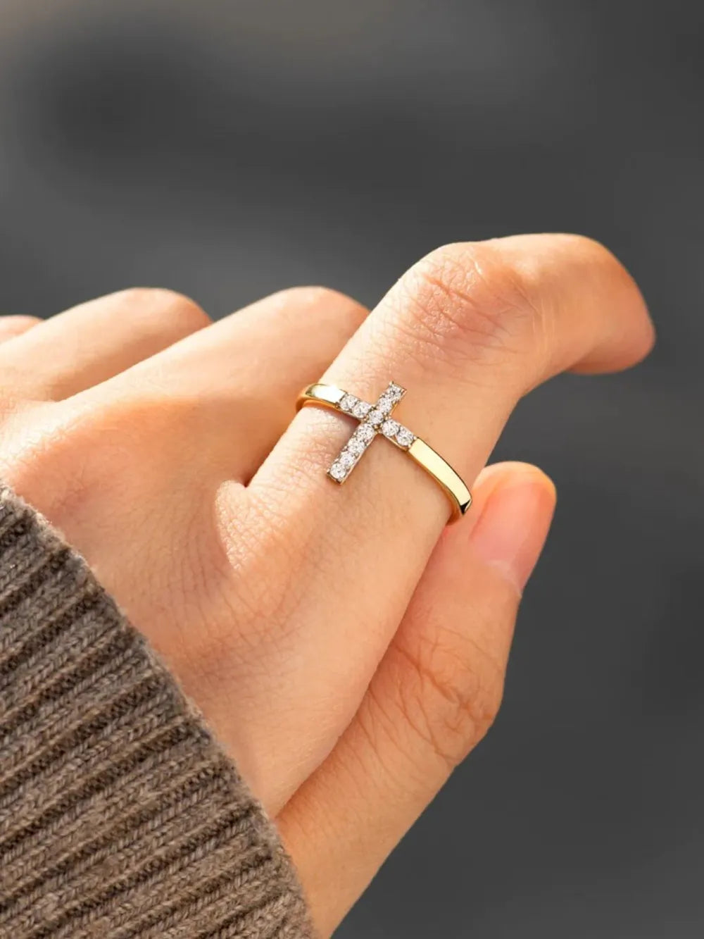 Gold band ring with a pavé crystal cross detail on a hand.