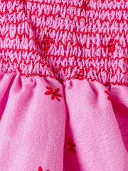 Pink cotton baby dress with smocked bodice and red floral print skirt.